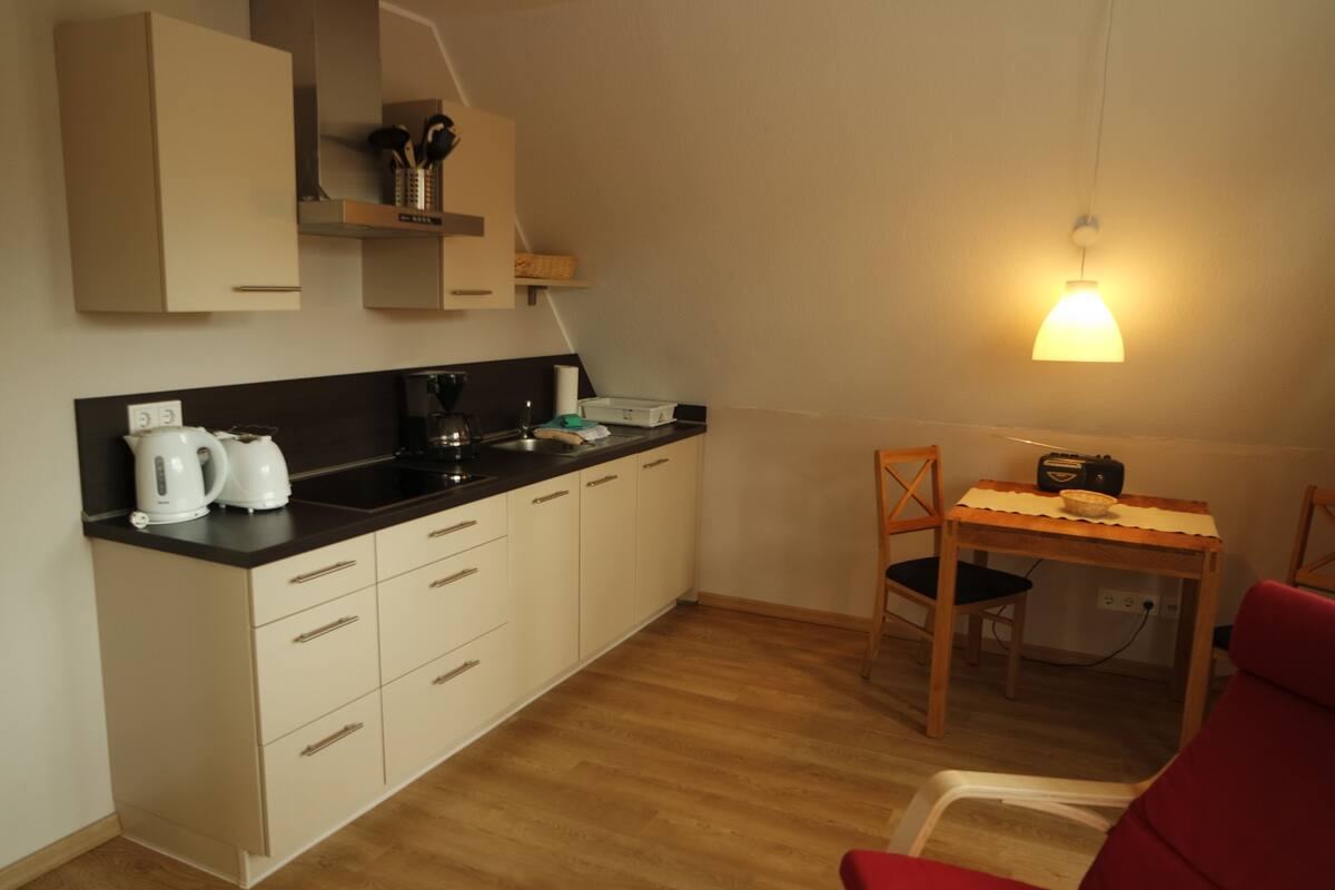 A compact kitchen with white cabinets, a black countertop, and a wooden dining table with chairs.
