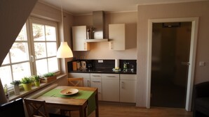 Eine kleine Küche mit Essbereich, ein Fenster mit Pflanzen und eine Tür zu einem weiteren Zimmer.