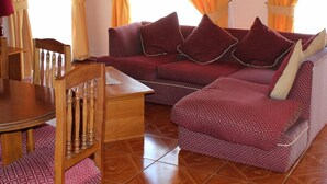 Ein Wohnzimmer mit einem Holzespeisetisch, einem Holzstuhl, einer Couch mit gemusterten Kissen und orangefarbenen Vorhängen.