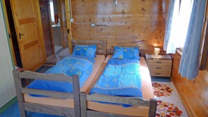 Ein Holzhütten-Zimmer mit zwei Betten, einem Nachttisch, einer Lampe und einem Fenster mit Vorhängen.