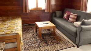 Ein gemütliches Zimmer mit Holzboden, einem gemusterten Teppich, einer Couch, einem kleinen Tisch und einem Bett.
