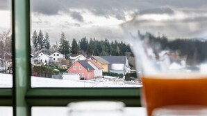 A view of a residential area with houses and trees through a window, with a glass of orange juice in the foreground. - Bergliebe (G 103) by Interhome (Dittishausen)