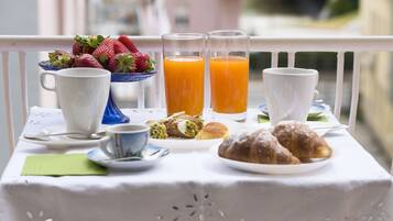 A breakfast table with a white tablecloth, a bowl of strawberries, two glasses of orange juice, a cup of coffee, a plate with pastries, and a green napkin.