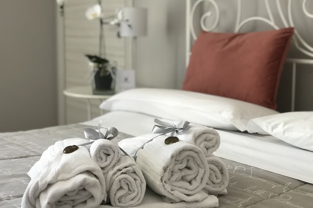 A neatly made bed with white linens, a red pillow, and rolled towels with a bow.