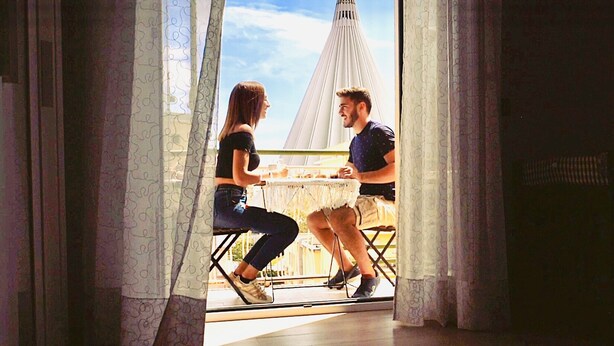 Dos personas sentadas en un balcón con vistas a una estructura blanca que recuerda a una torre.