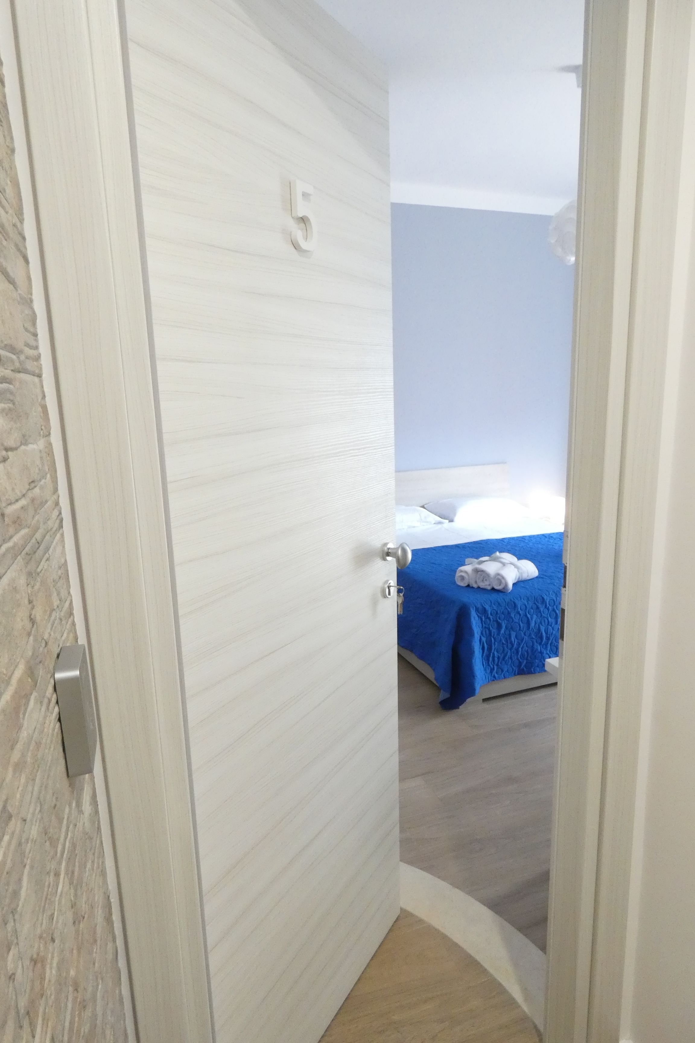 A hotel room with a bed, a blue bedspread, and a number '5' on the door.