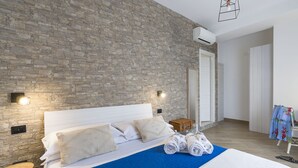 Una habitación de hotel moderna con pared de piedra, cama bien hecha con cubrecama azul y cómoda de madera.