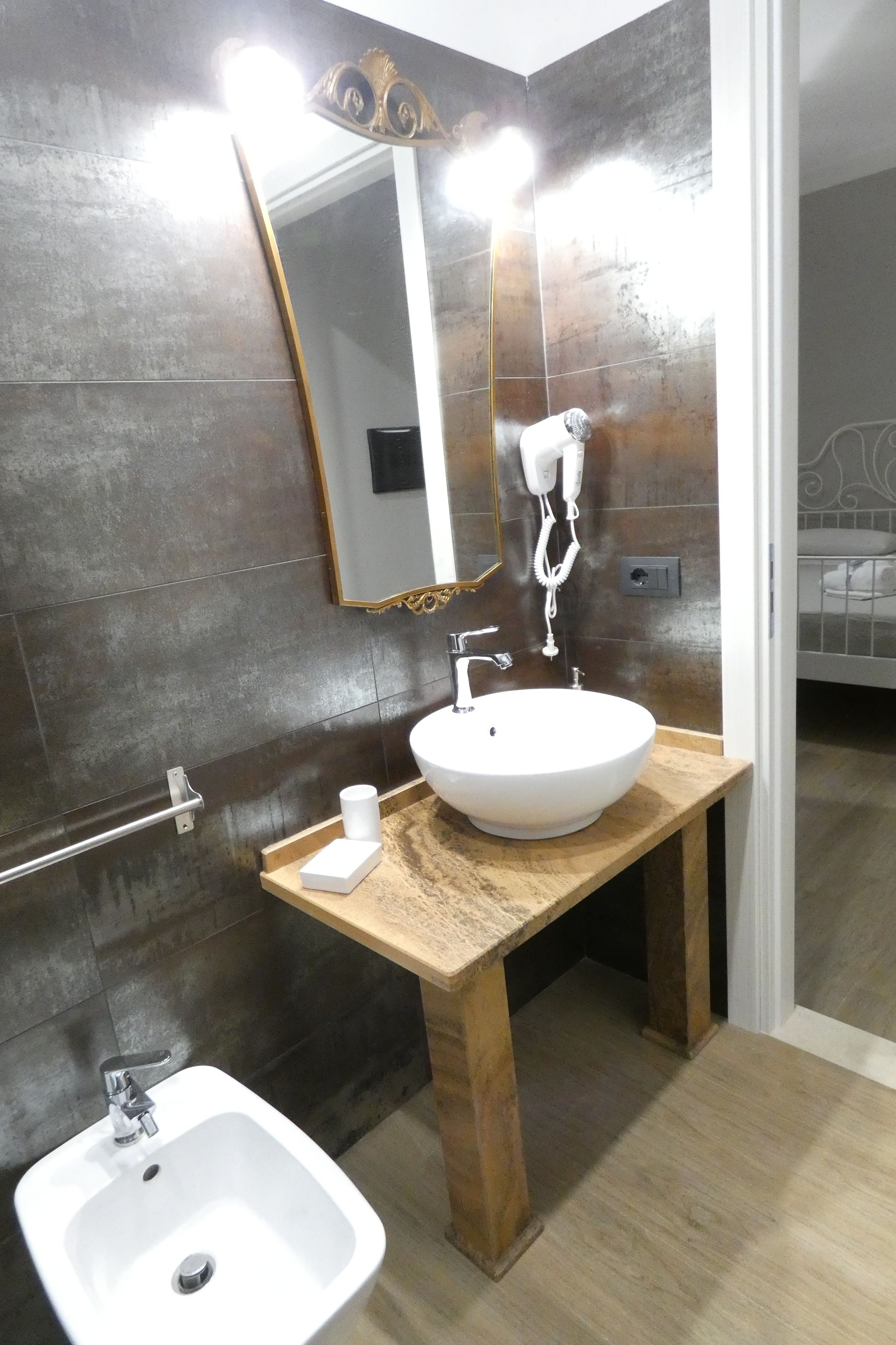 Un baño con tocador de madera, lavamanos blanco, espejo con iluminación y secador de mano.