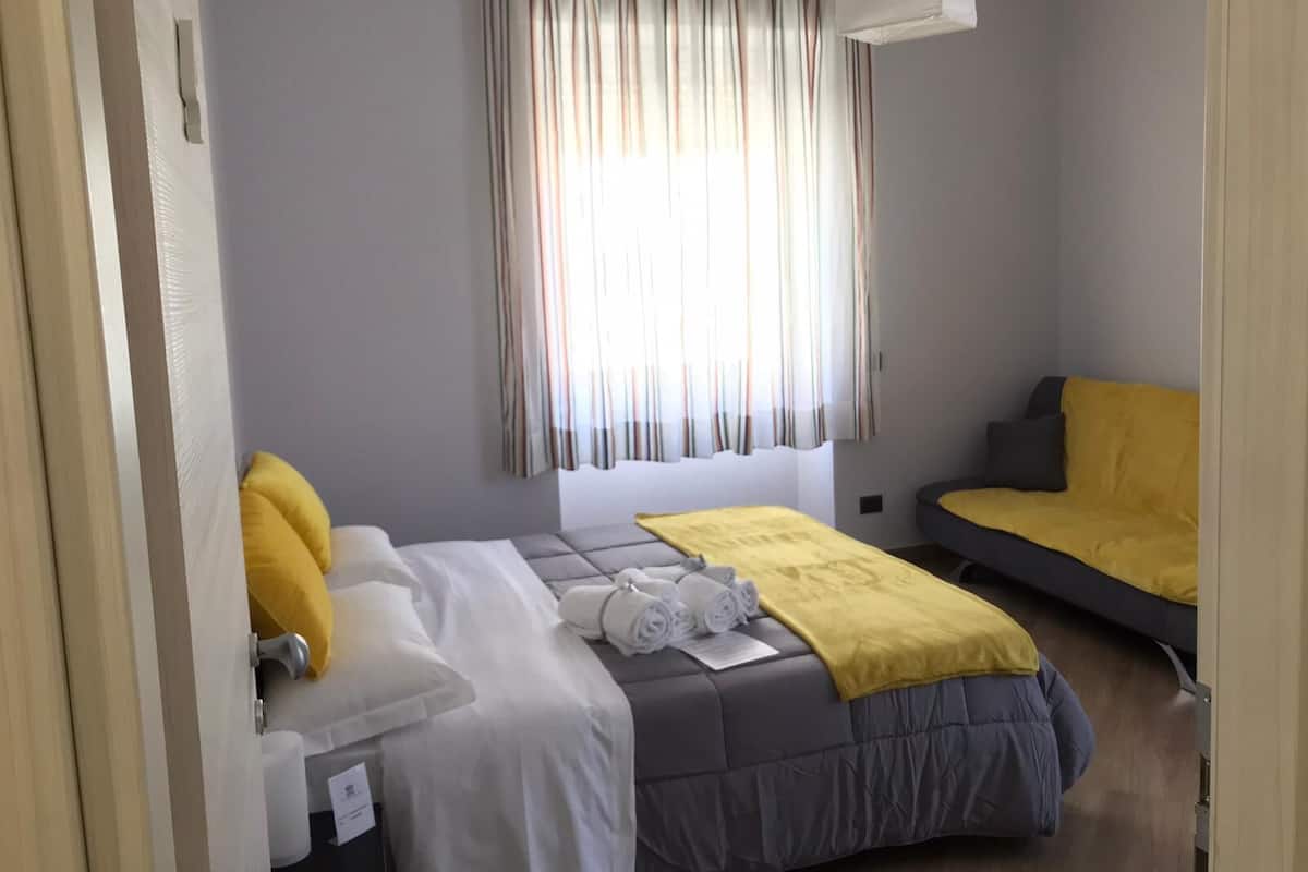 A bedroom with a bed, a sofa, and a window with curtains.