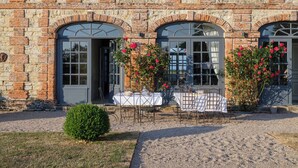 A stone building with arched windows and a gravel courtyard with tables and chairs. - Le Domaine de Ravenoville (Sainte-Mere-Eglise)