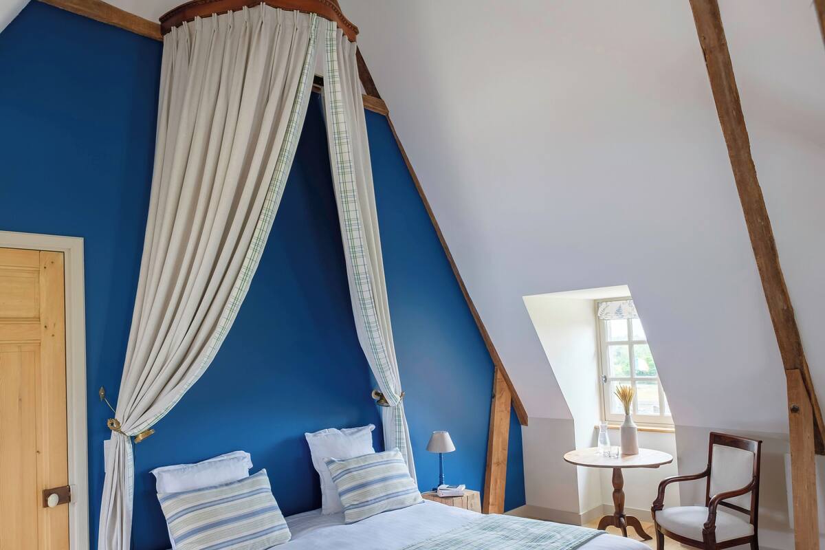 Una camera da letto con un letto a baldacchino, pavimento in legno, parete blu e una finestra che lascia entrare luce naturale.