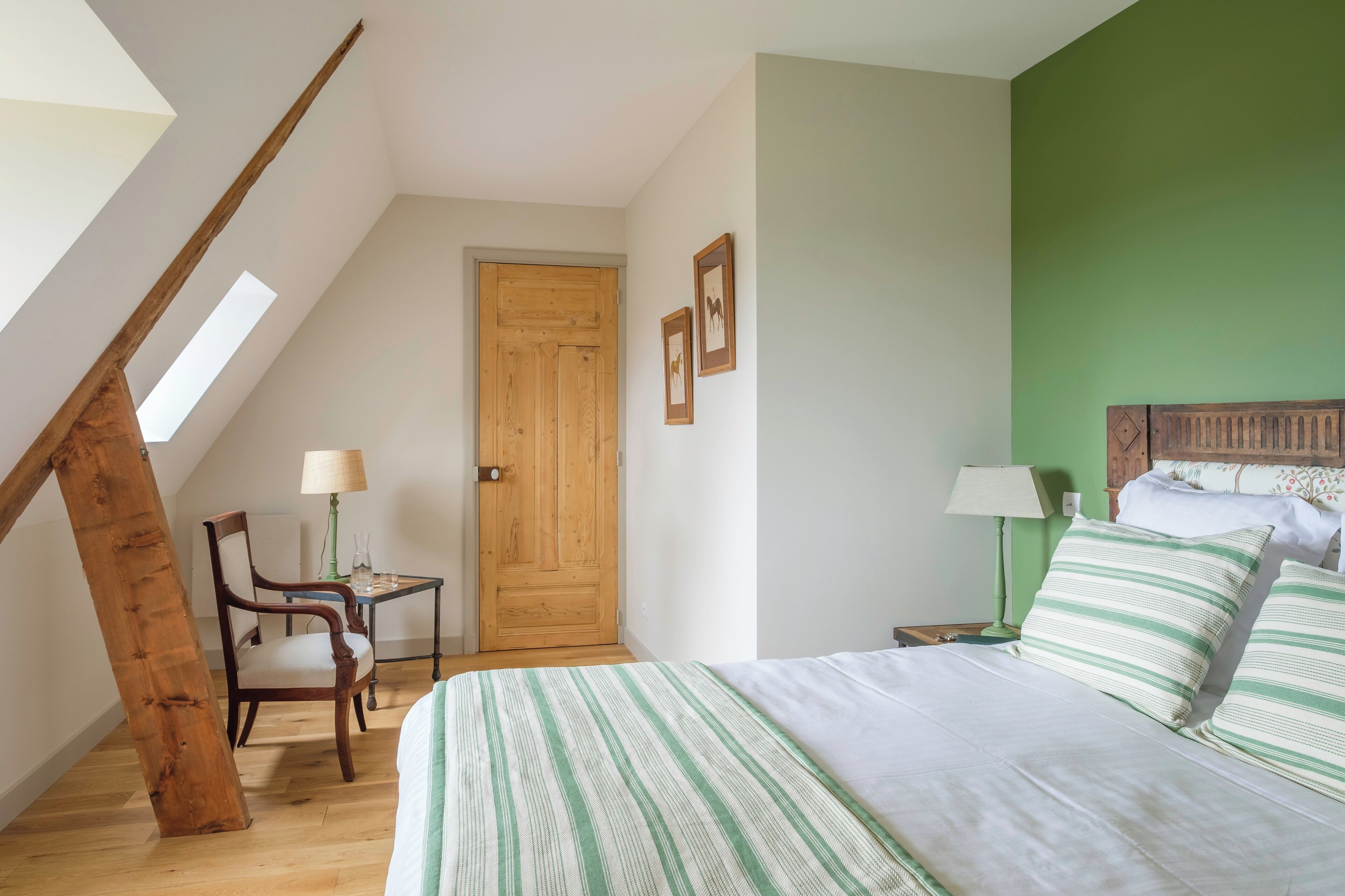 A bedroom with a bed, a wooden chair, a small table, a lamp, and a door.