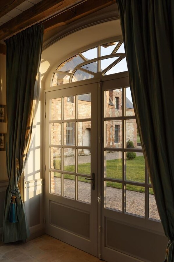 A room with a large arched window, a wooden ceiling, and a view of a stone building outside.