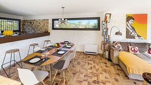 A dining area with a table set for four, a kitchen with a fruit bowl, and a bookshelf with books. - La Maison du Midi by Interhome (Les Issambres)