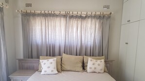 A bedroom with a bed, two pillows, a nightstand, and a wardrobe. - Pachigomo Guest House (Goromonzi)