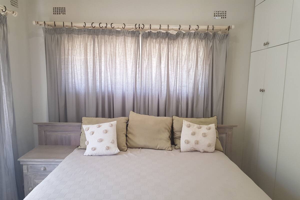 A bedroom with a bed, two pillows, a nightstand, and a wardrobe.