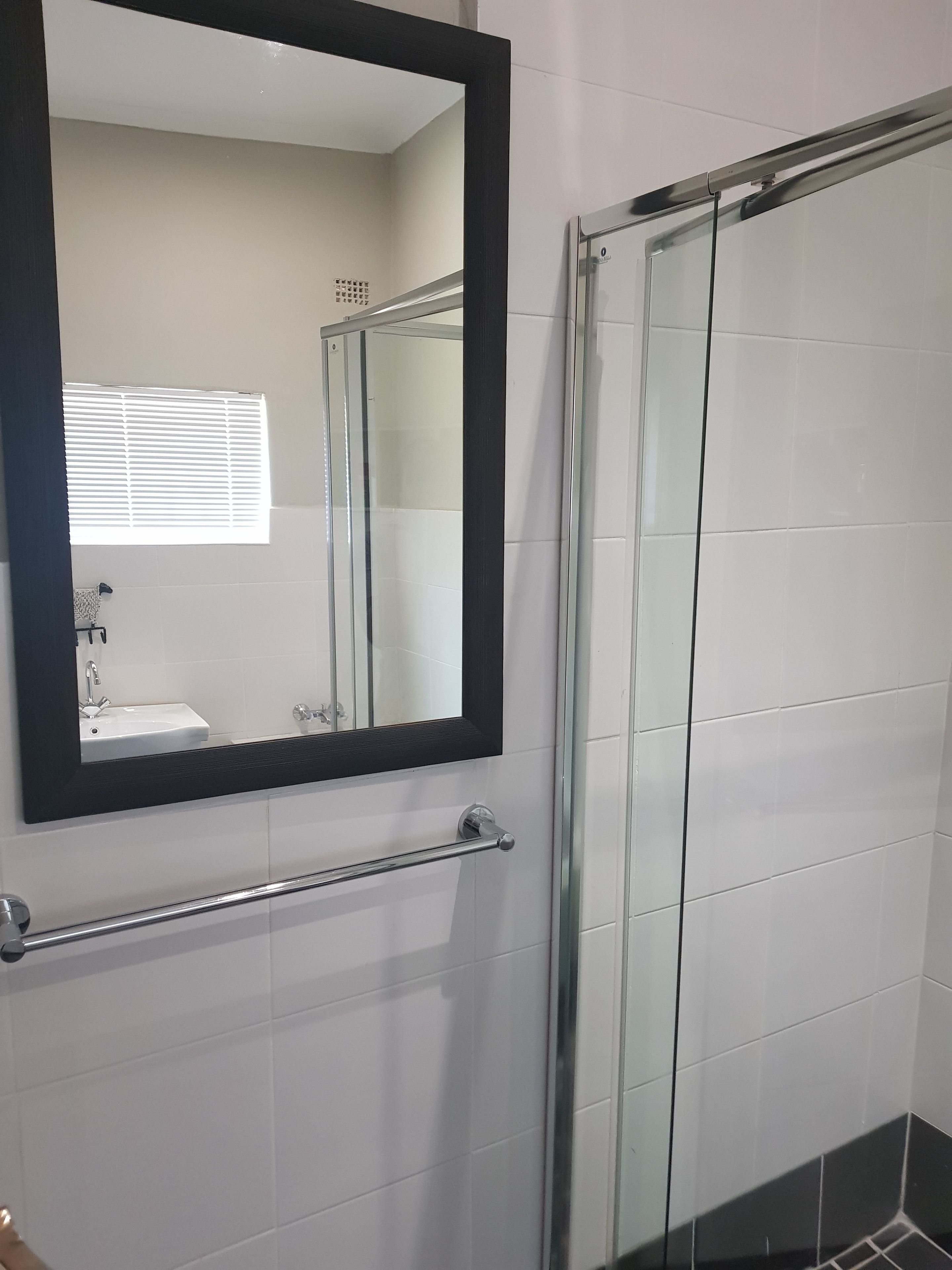 A bathroom with a glass shower enclosure, a white sink, and a mirror with a black frame.