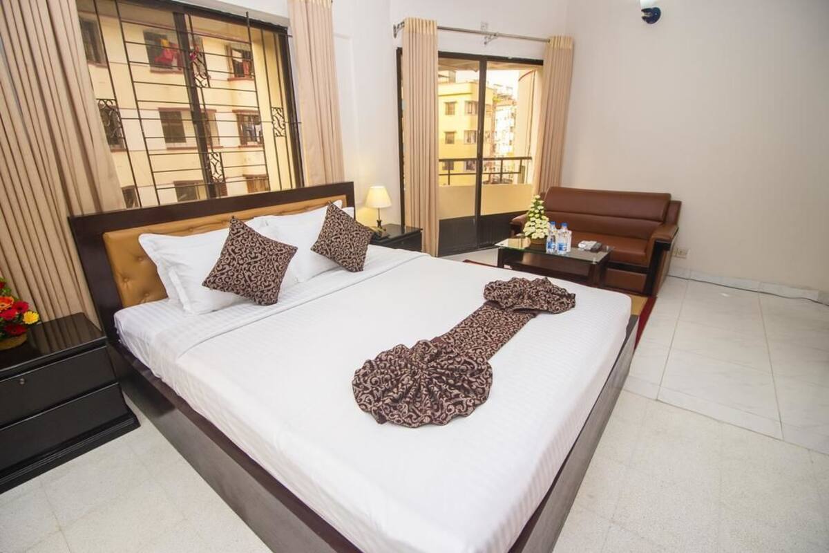 A hotel room with a large bed, a nightstand, a sofa, and a view of the outside.