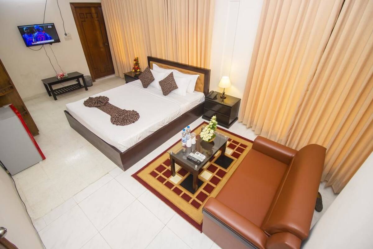 A hotel room with a bed, a sofa, a TV, and a small table with a flower vase.