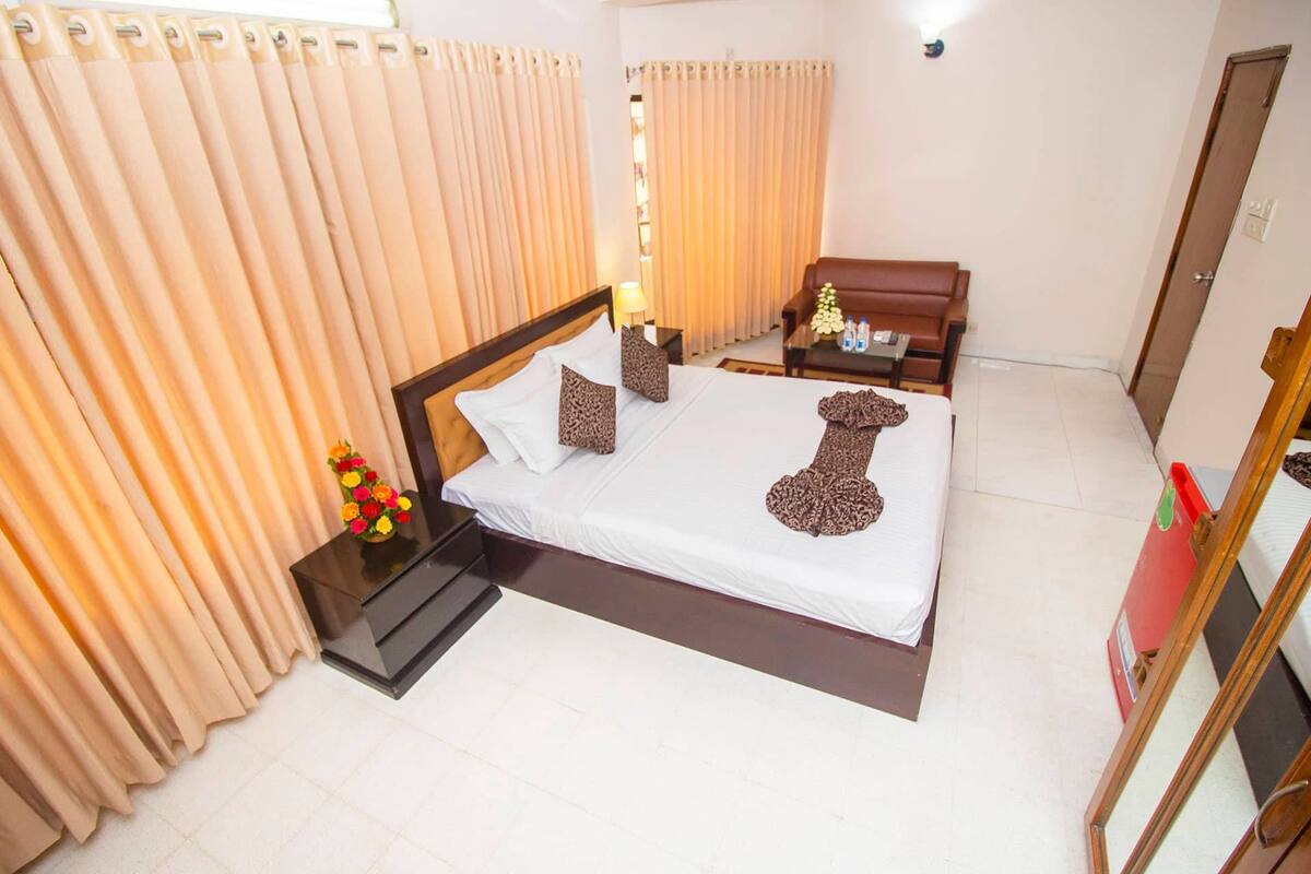 A hotel room with a bed, curtains, a nightstand, a table, and a mirror.