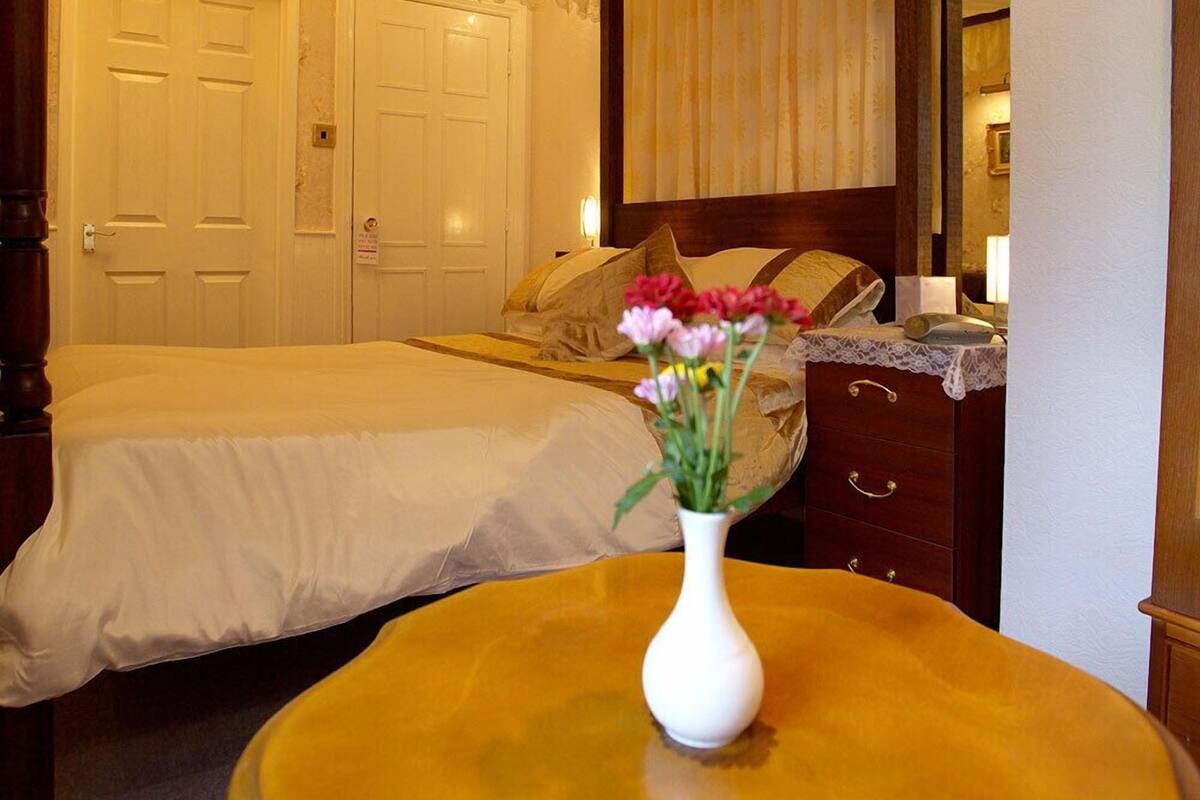 Habitación de hotel con dos camas, un aparador de madera, una tocador con espejo y un florero con flores sobre una mesa redonda.