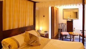 A hotel room with a large bed, a wooden headboard, a bedside table with a lamp, a chair, a small table with a vase, and a mirror on the wall. - Moonraker House (Stratford-upon-Avon)
