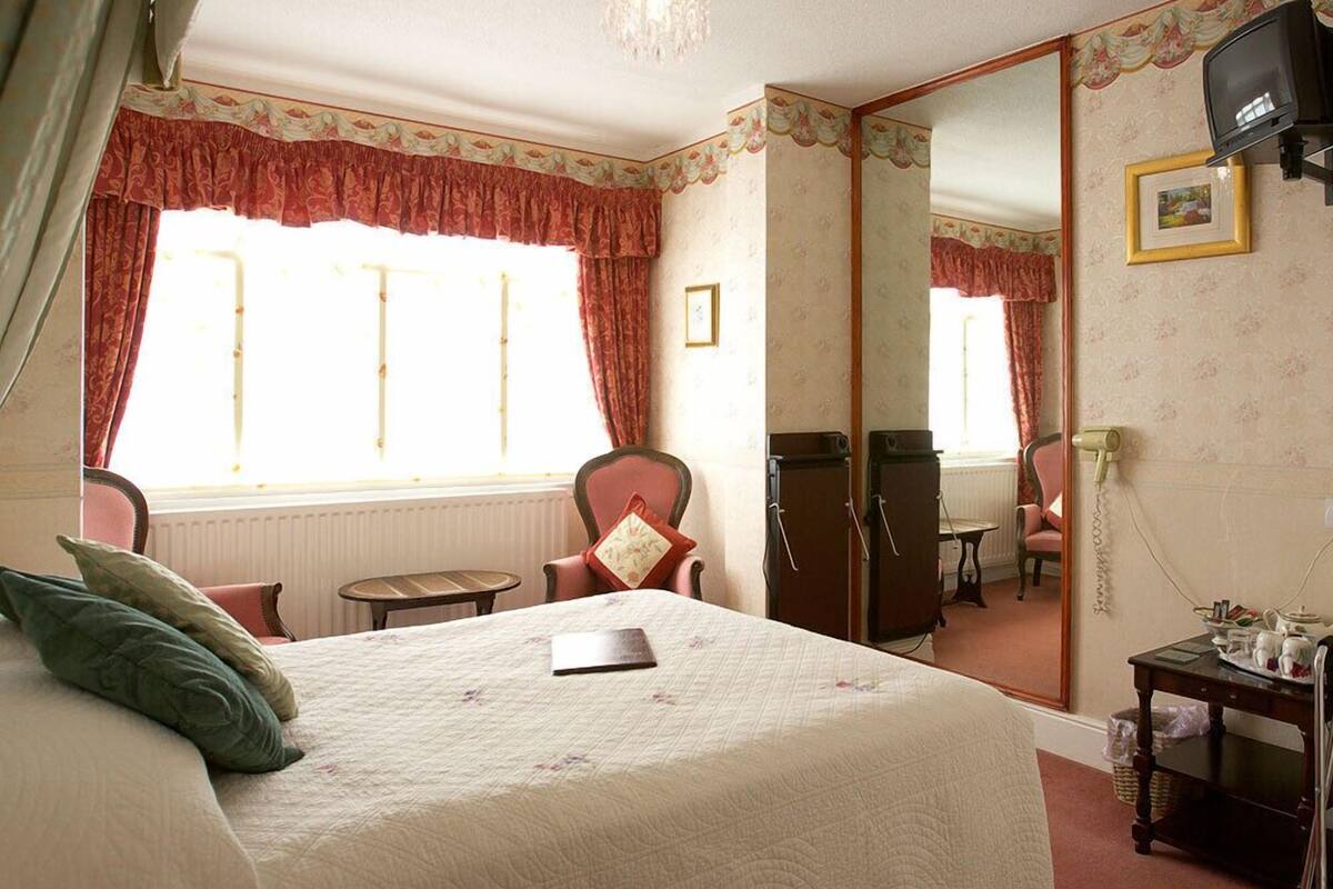 Un dormitorio con cama, una silla, un escritorio, un espejo y una televisión.