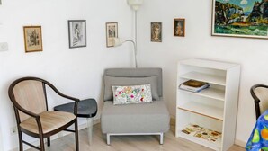 Une pièce comprenant un fauteuil gris, une chaise en bois, une bibliothèque blanche et un lampadaire.