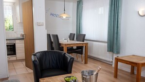 Ein modernes Wohnzimmer mit einem Holzesstisch, einem schwarzen Ledersessel und einem kleinen Holztisch mit Käse und Weingläsern.