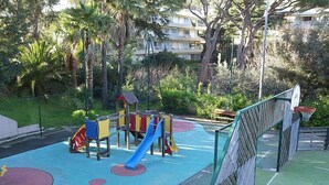 A playground with a slide and climbing structures, surrounded by greenery and a fence. - Villa Francia by Interhome (Cannes)