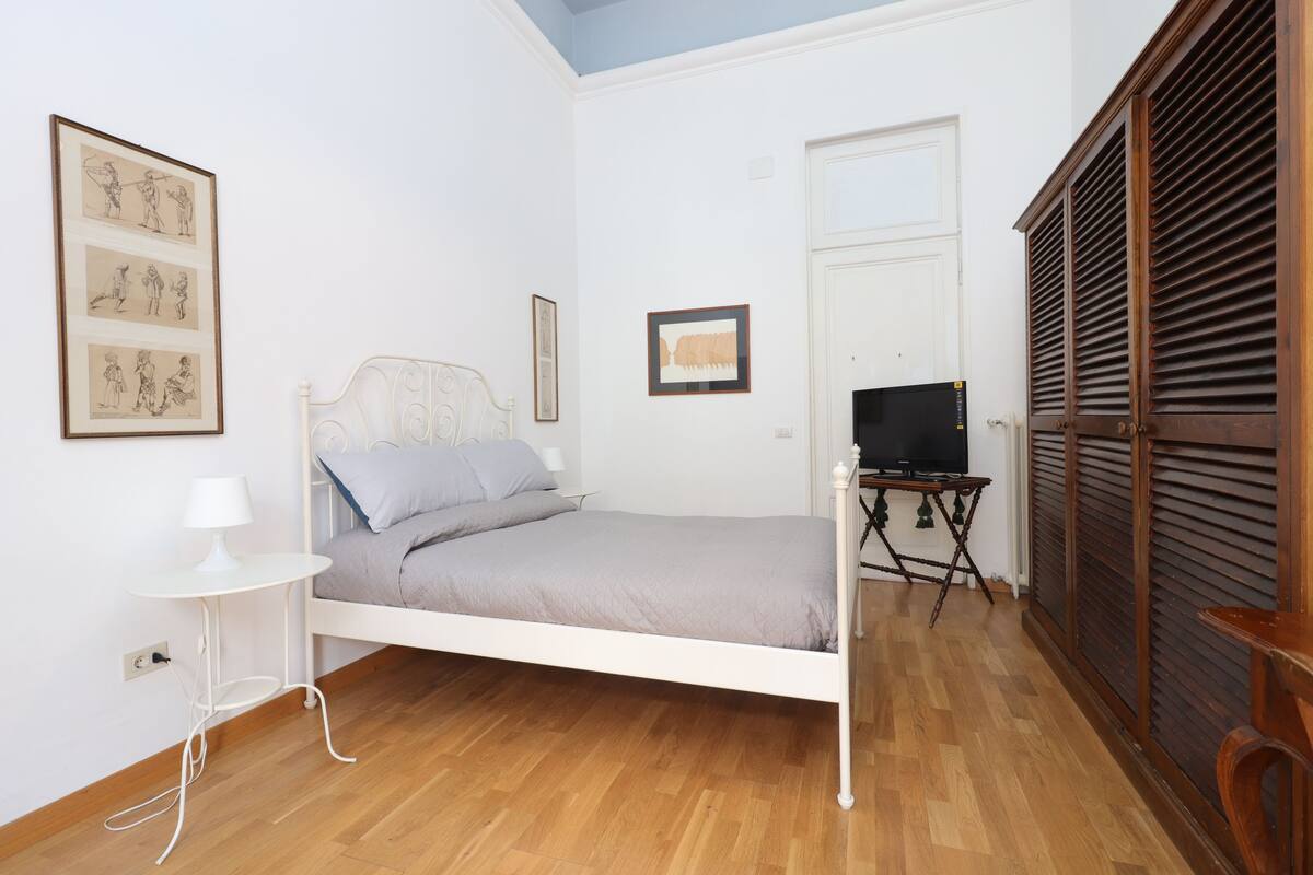 Une chambre à coucher avec un lit, un téléviseur posé sur un meuble, une petite table avec une lampe et une armoire.