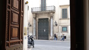 A street view with a large wooden door, a motorbike parked on the side, and pedestrians walking on the sidewalk. - Trevi suites B&B (Rome)