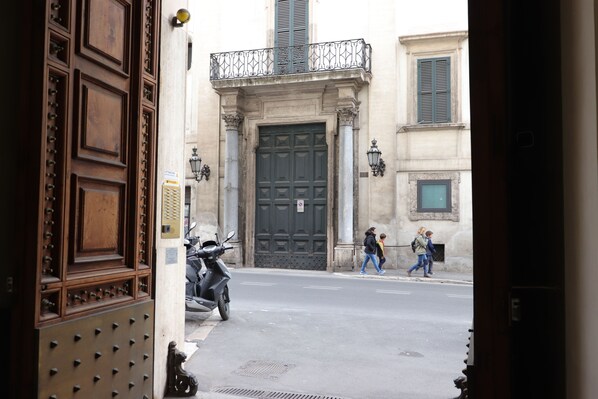 A street view with a large wooden door, a motorbike parked on the side, and pedestrians walking on the sidewalk. - Trevi suites B&B (Rome)