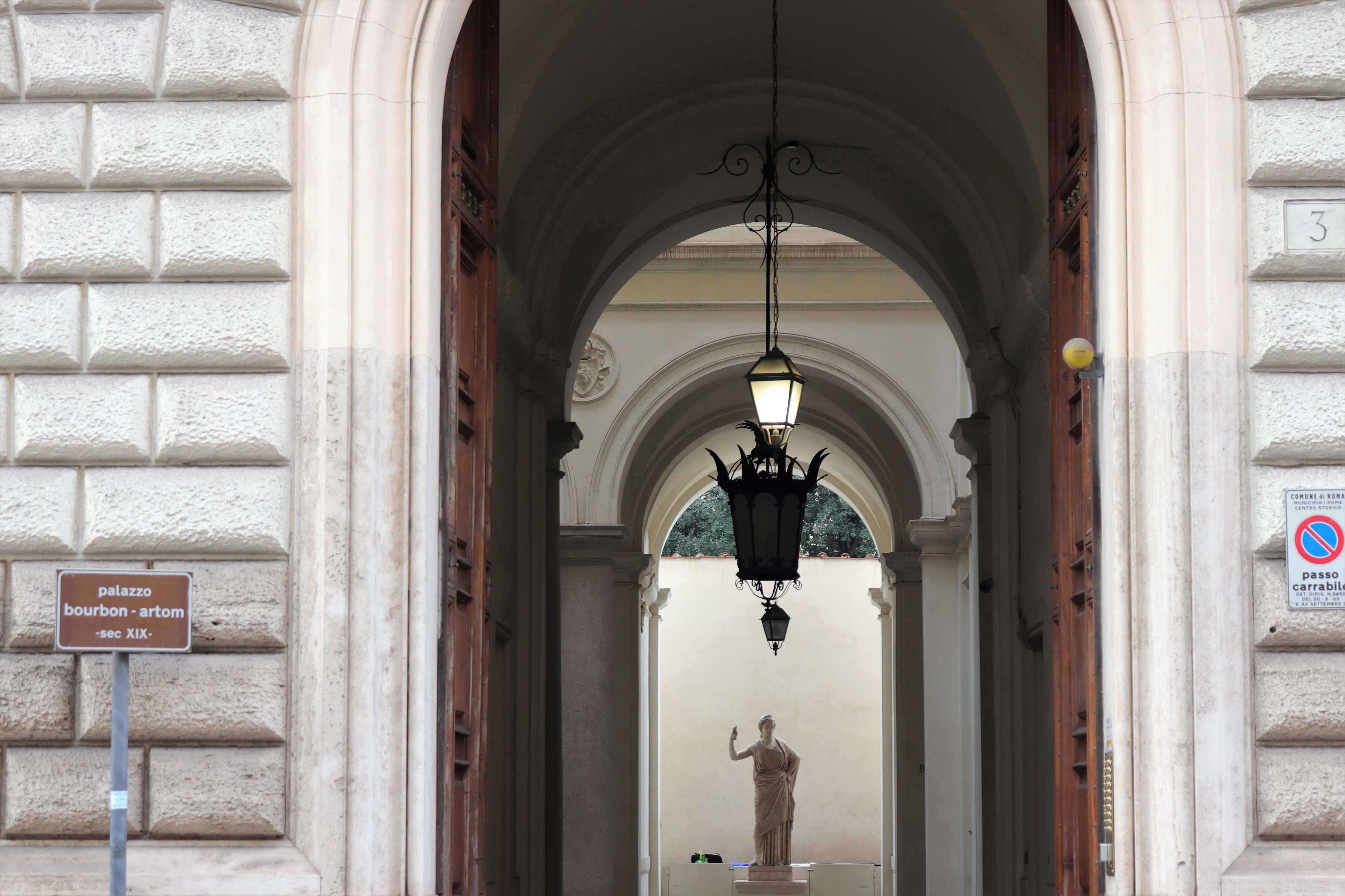 An arched entrance with a statue, a hanging lantern, and a sign indicating a historical building.