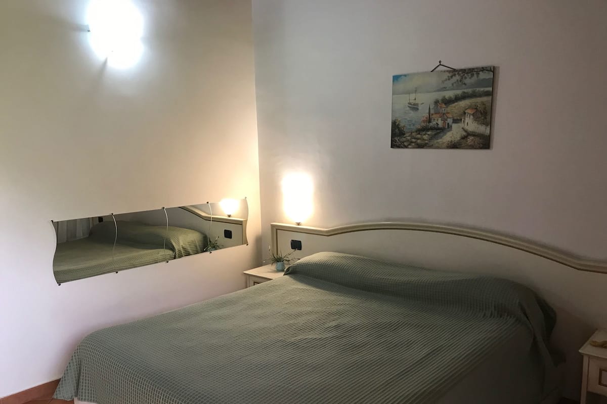Une chambre à coucher comprenant un lit, une table de chevet, une commode, un miroir fixé au mur et un tableau.