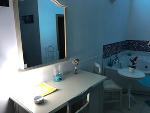 A bathroom with a bathtub, sink, and mirror. There is a chair and a table with a vase and a book. - Motel 24h (Lusciano)