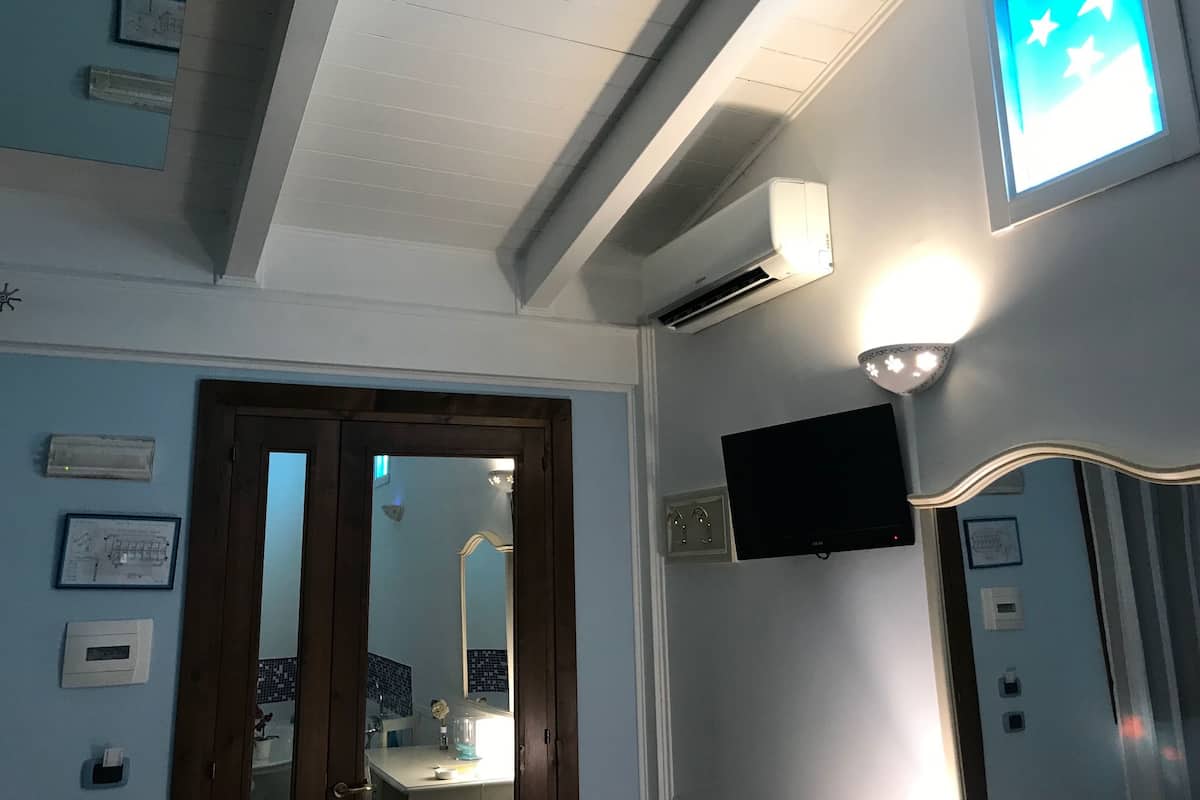 Une salle de bain avec un miroir, un lavabo, des toilettes et une douche. On y trouve également un ventilateur de plafond, un luminaire et un téléviseur fixé au mur.