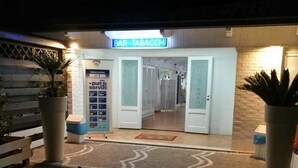 An outdoor seating area with a table and chairs, a potted plant, and a bar entrance with a sign reading "BAR TABACCHE". - Motel 24h (Lusciano)