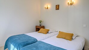 Habitació d'hotel amb dos llits, cadascun amb llençol blau i blanc, i una petita taula de nit de fusta amb un ram de flors.