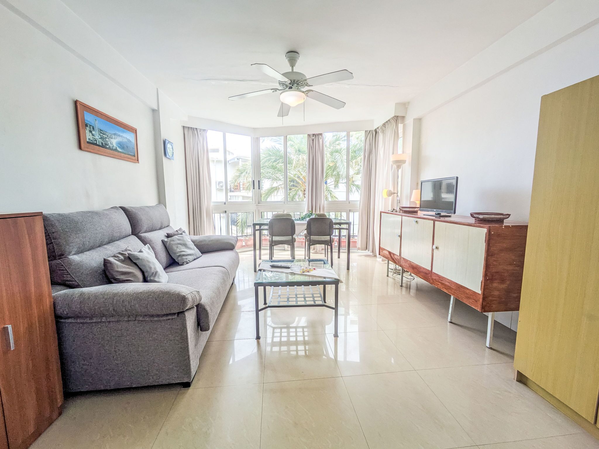A modern living room with a sofa, a glass coffee table, and a TV on a wooden cabinet.