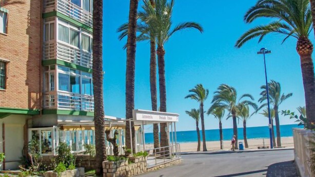 Un hôtel situé en bord de mer, doté d’une entrée imposante, de palmiers et offrant une vue dégagée sur l’océan.
