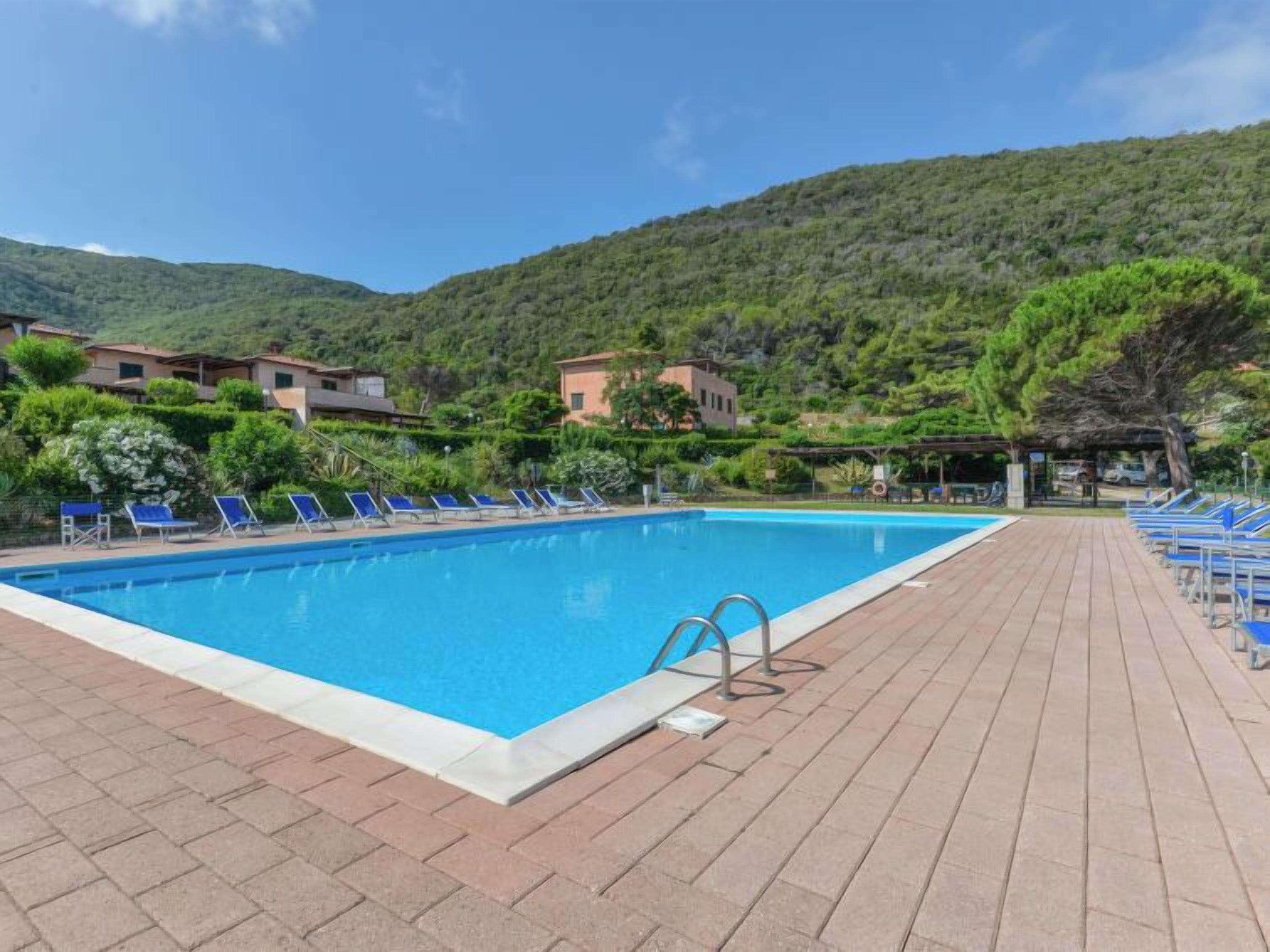 A swimming pool with lounge chairs, surrounded by buildings and greenery.