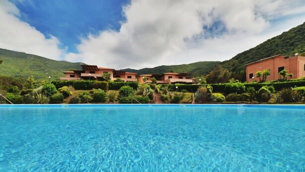 Una piscina azul cristalina con vistas a un edificio de resort de varios pisos y un telón de fondo montañoso.