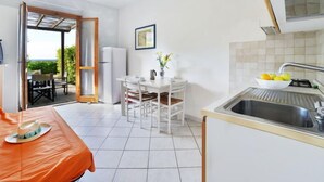 Una cocina compacta con lavamanos, una zona de comedor con mesa y sillas, y vista a través de una puerta abierta hacia un espacio exterior con asientos.