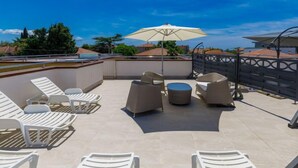 A rooftop patio with white lounge chairs, a round table, and a large umbrella. - Villa Alpa by Interhome (Umag)