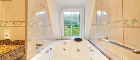 A large, freestanding bathtub in a bathroom with a view of greenery outside.