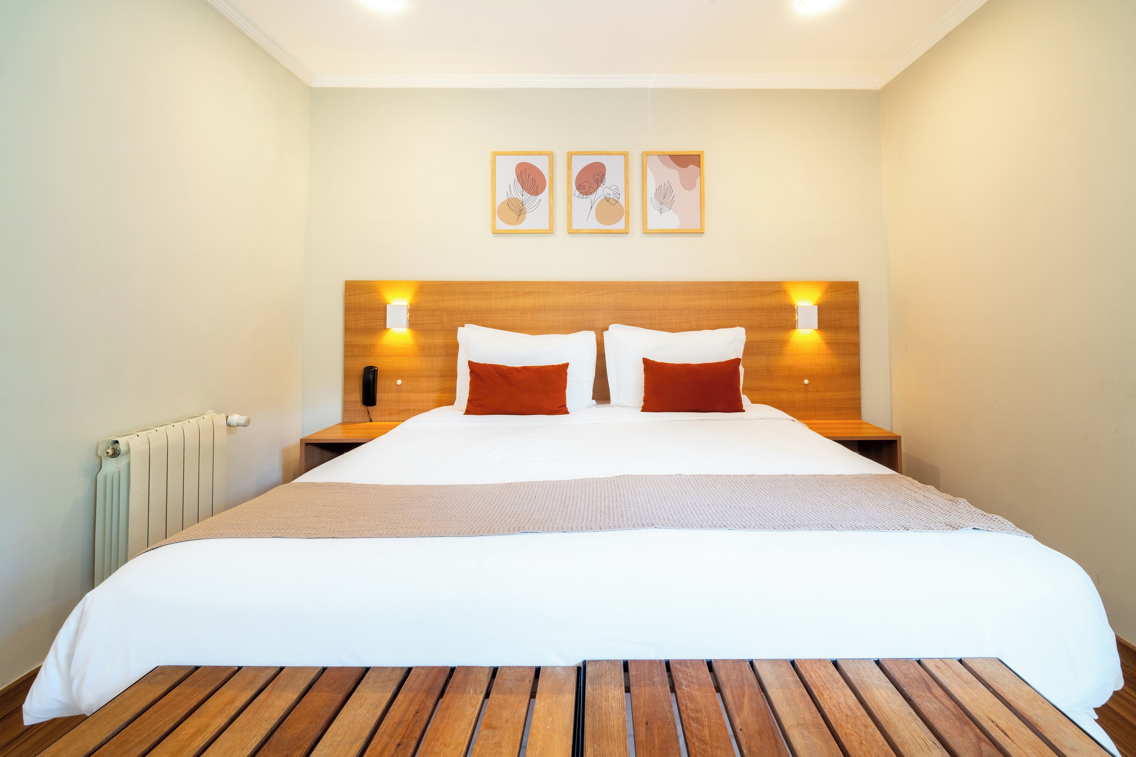 A neatly made bed with white and red bedding, wooden headboard, and bedside lamps.