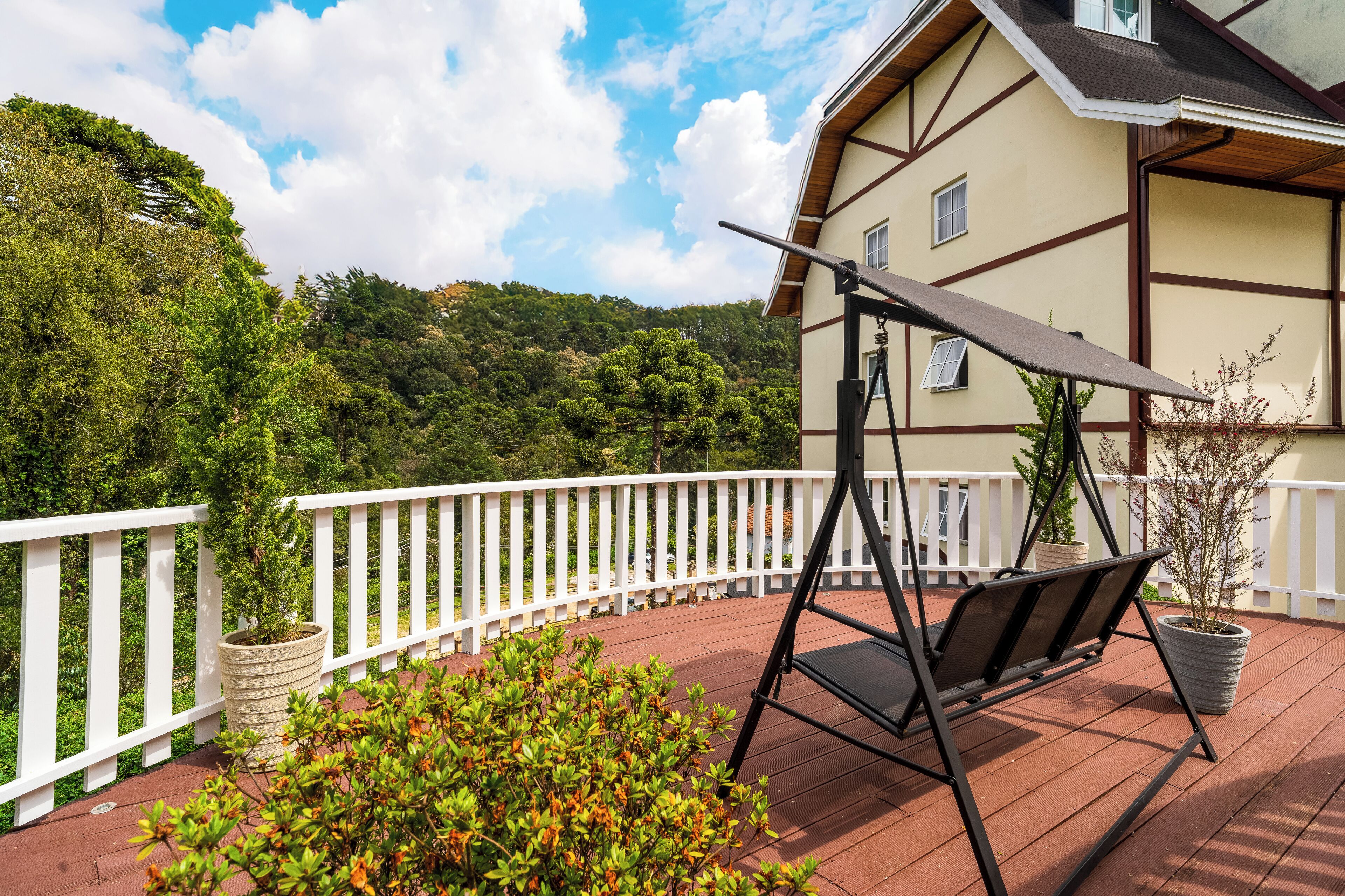 A wooden deck with a swing chair, white railing, and potted plants.
