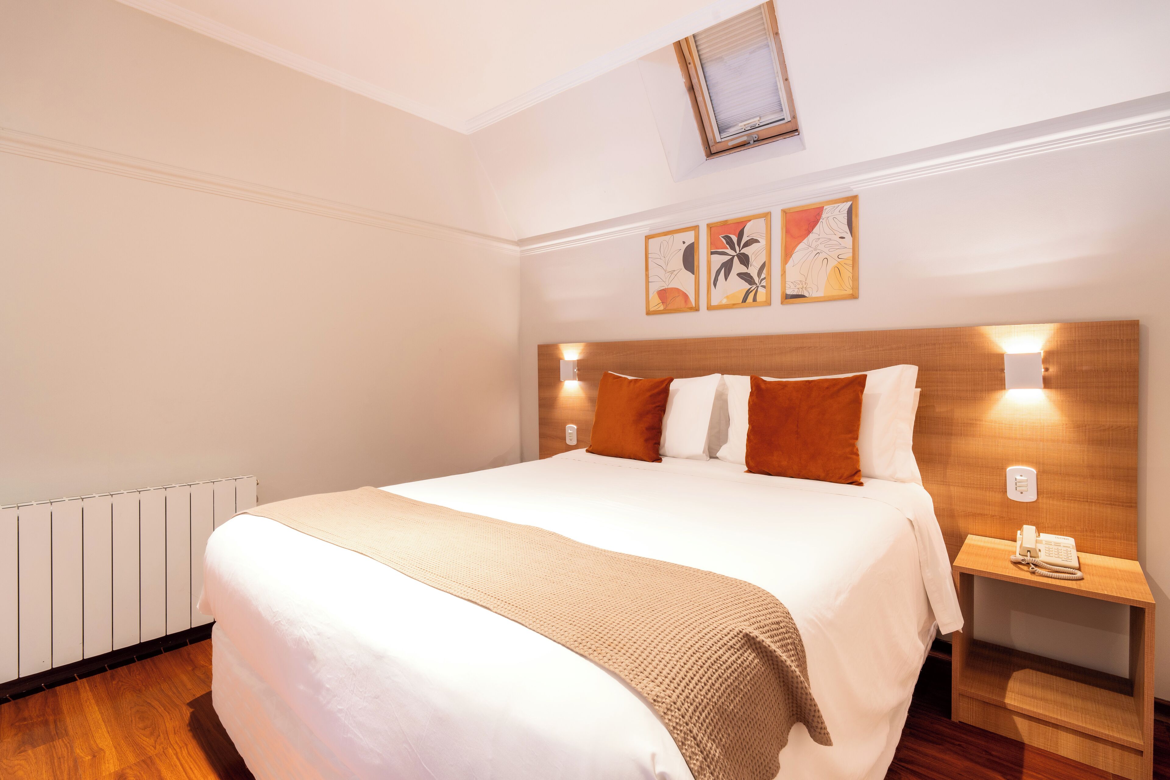 A neatly made bed with a beige blanket, a wooden headboard, and two bedside lamps.