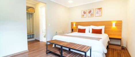A modern hotel room with a wooden floor, a large bed with white bedding, a wooden bench, and artwork on the wall.